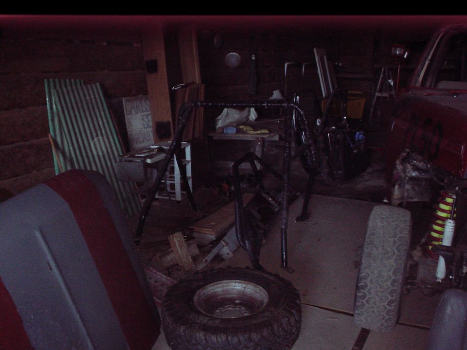 roll cage and spare tire in a cluttered garage with a red vehicle fender visible