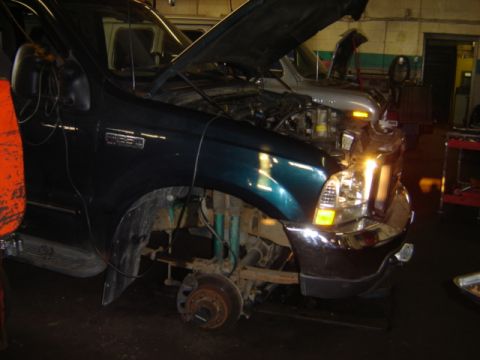 1992 Ford Bronco - A dark green truck is in a garage with its hood open, undergoing mechanical work on the front end and suspension.