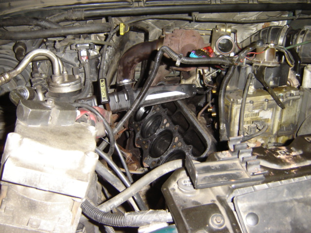 Engine bay with cylinder head removed, showing pistons and engine block. Some hoses and wiring are visible