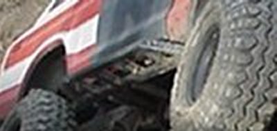 1979 Ford Bronco - A red and white striped truck is shown from the side, with a focus on its large off-road tires and suspension system.