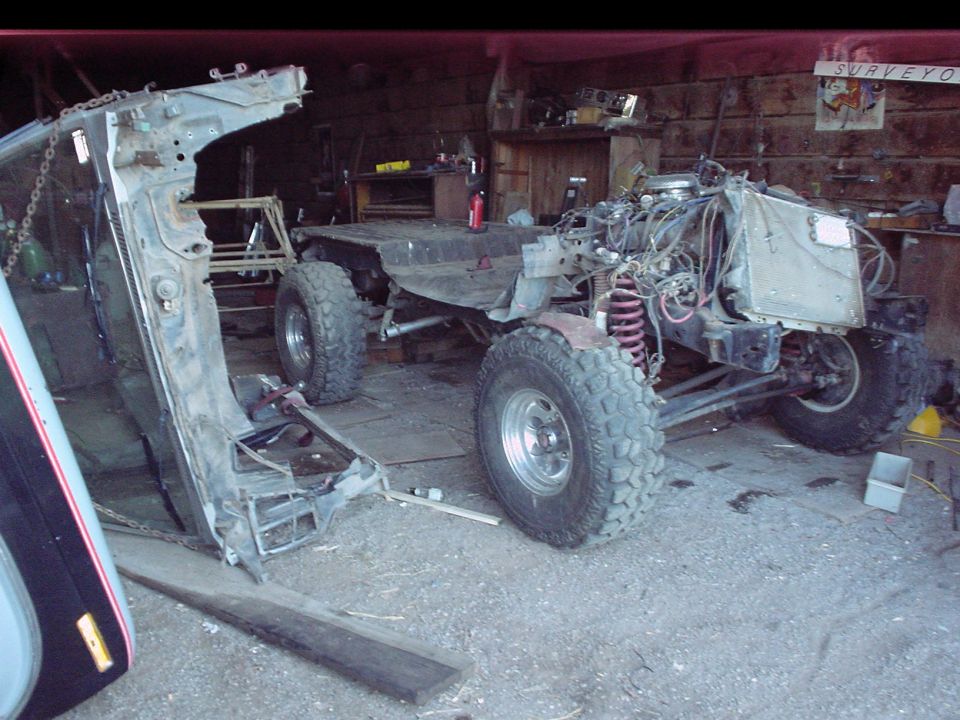 Bare truck frame on tires with engine and suspension installed, body off, in a wooden garage