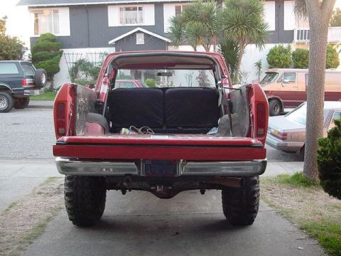 1979 Ford Bronco - Rear view of a red 1979 Ford Bronco parked in a driveway with other vehicles visible.