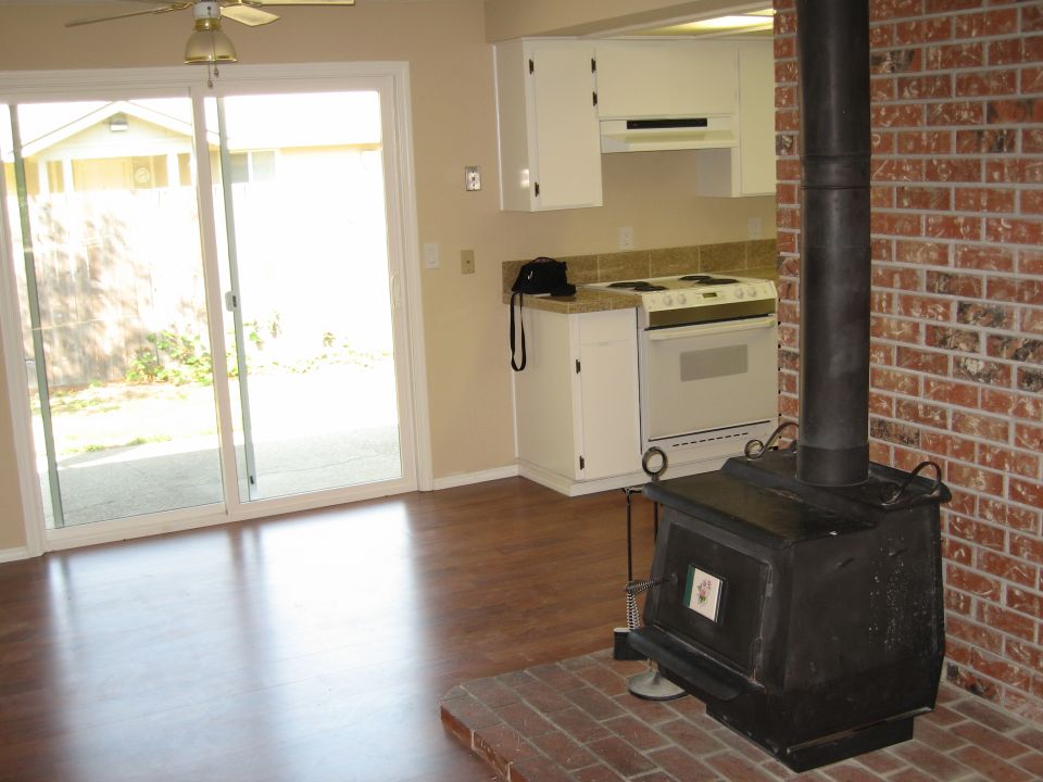 Interior view of a house with a wood-burning stove, kitchen appliances, and sliding glass doors