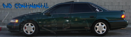 1993 Ford Taurus - A dark green sedan is parked in front of a brick wall with blue graffiti.