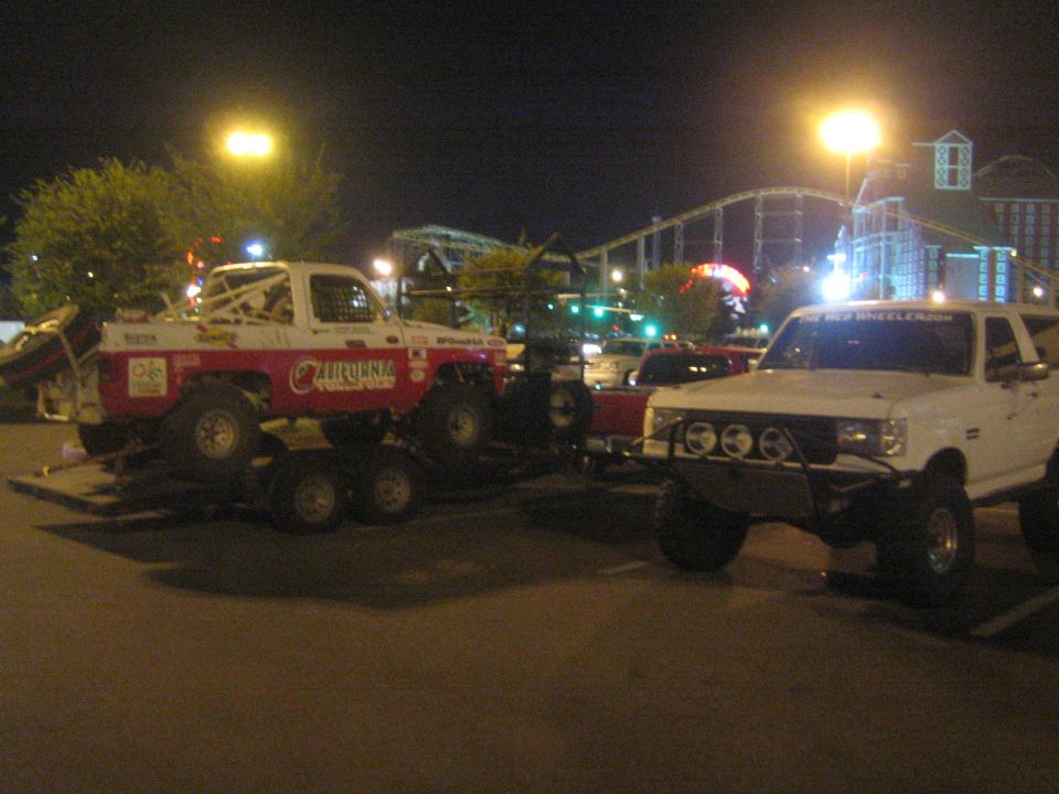 White lifted truck next to red California race truck on trailer at night