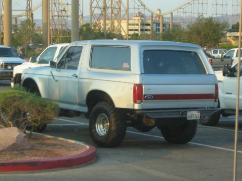 1990 Ford Bronco - lifted white full-size Ford Bronco with an extended fiberglass roof sits in a parking lot beside other trucks at dusk.