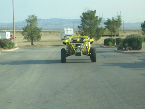 1990 Ford Bronco - yellow tube-frame sand rail buggy sits on pavement with desert scrub and distant mountains in the background.