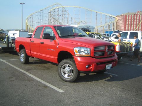 1990 Ford Bronco - red Dodge Ram crew-cab pickup with chrome wheels parks in a lot near a roller coaster and a large red building.