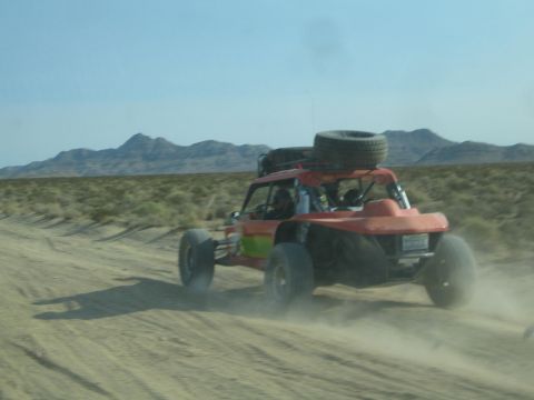 1990 Ford Bronco - orange and green open-cockpit race buggy with a roof-mounted spare kicks up dust racing across the desert.