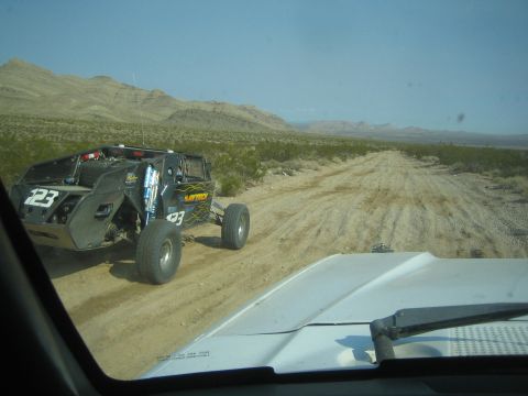1990 Ford Bronco - black off-road race buggy numbered 123 travels along a rutted desert dirt road past scrub brush.