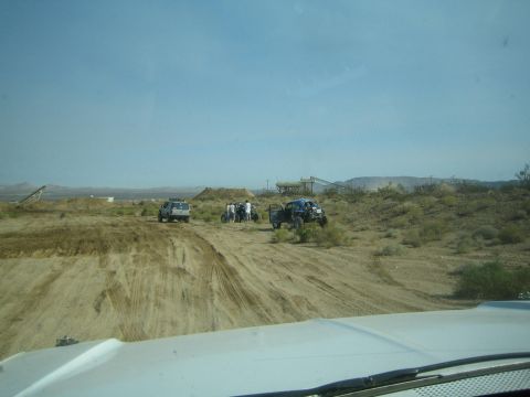 1990 Ford Bronco - group of off-road vehicles including a blue buggy and white truck cluster on a desert hillside near earthworks.