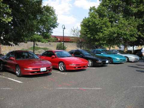 1997 Ford Probe - A line of Ford Probe cars, including two red ones, a black one, a teal one, and a silver one, are parked in a lot.
