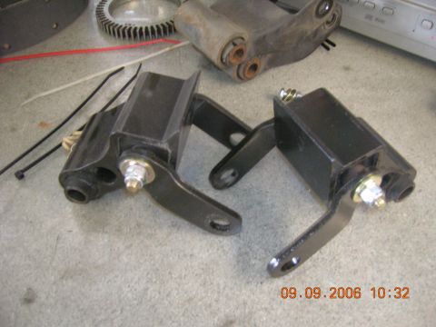 1996 Ford Bronco - Two black suspension parts are shown on a concrete surface with other miscellaneous items in the background.