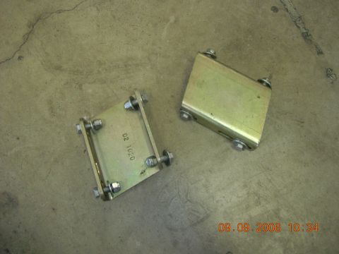 1996 Ford Bronco - Two metal brackets with visible bolts and markings sit on a concrete surface.