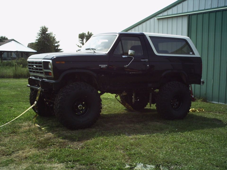 Black 1986 Ford Bronco lifted with large tires, parked on grass