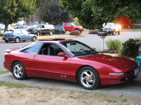 1997 Ford Probe - A red 1997 Ford Probe GT is parked in front of a house, with other cars visible in the background.