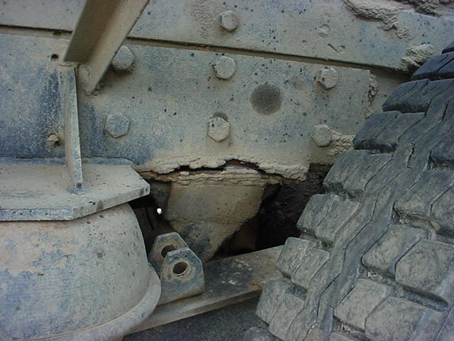 Close-up of a rusty truck suspension component with a tire tread visible