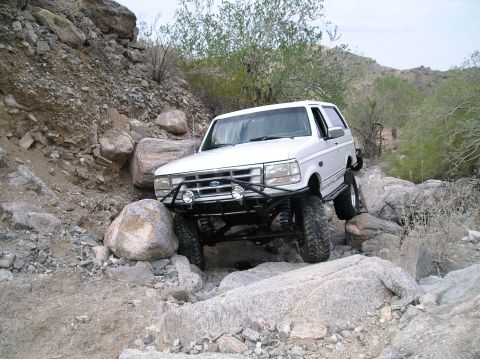 1993 Ford Bronco - A white Ford Bronco is shown off-roading on a rocky terrain.