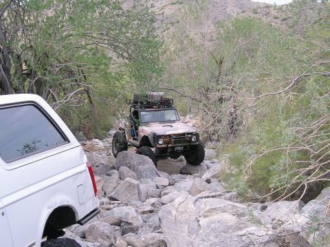 1993 Ford Bronco - Modified early Ford Bronco and a white SUV tackle a challenging rocky trail in a desert landscape.