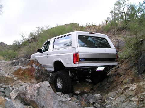 1993 Ford Bronco - White Ford Bronco is shown off-roading on a rocky hill.