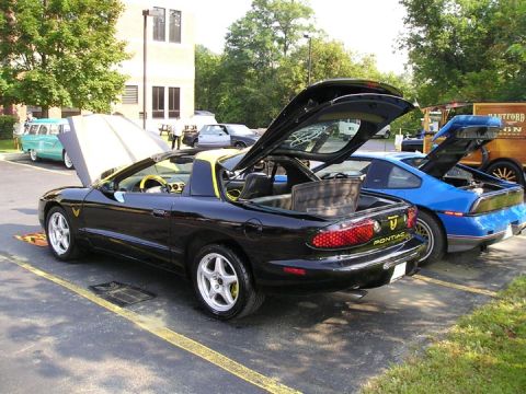 1984 Pontiac Fiero - A black 1994 Pontiac Trans Am convertible is parked next to a blue Pontiac Fiero, both with their trunks open.