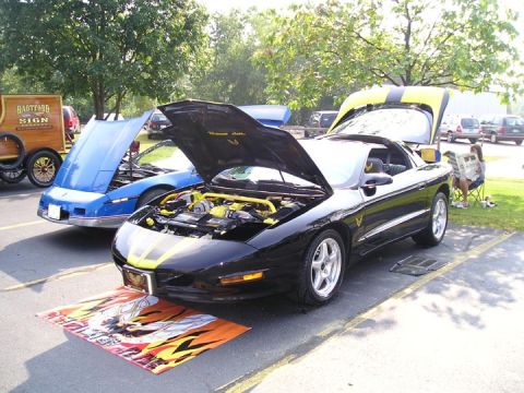 1984 Pontiac Fiero - Two cars with hoods open at an outdoor event. One is a black 1994 Pontiac Trans Am.