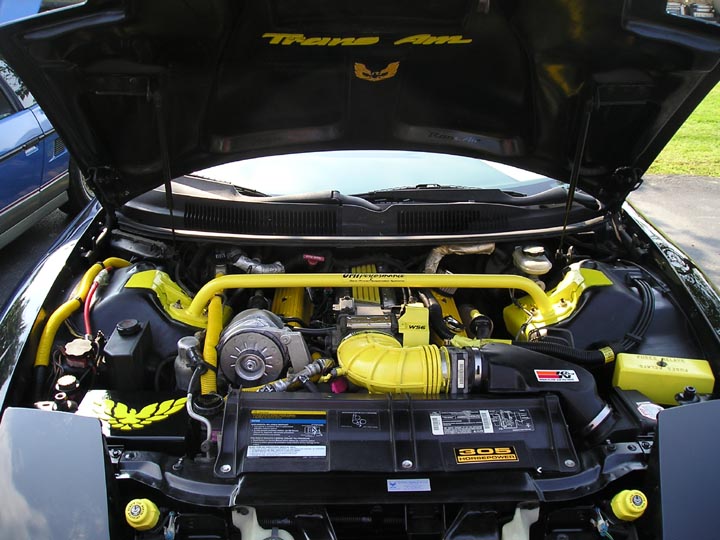 Engine bay of a 1994 Pontiac Trans Am with yellow accents and a strut bar