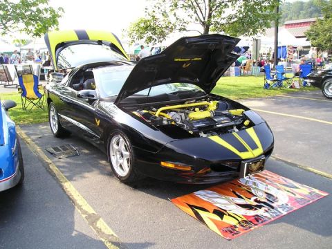 1984 Pontiac Fiero - A black 1994 Pontiac Trans Am with yellow accents and racing stripes is displayed with its hoods open at an outdoor event.