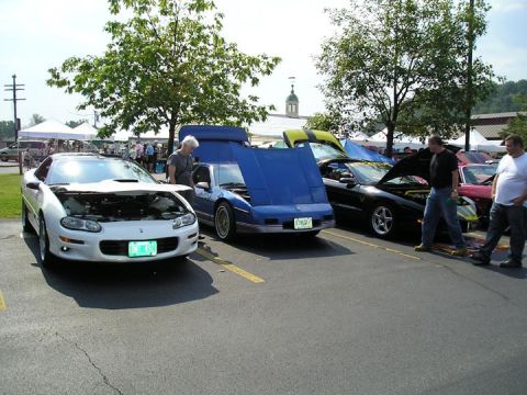 1984 Pontiac Fiero - Several cars are parked at an outdoor event, with their hoods open for display.