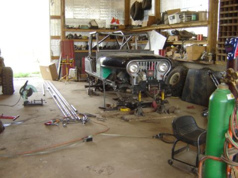 1992 Ford Bronco - A Jeep CJ-5 is in a state of disassembly and repair within a cluttered workshop environment.