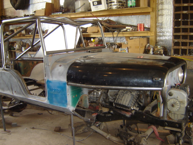Jeep CJ-6 body with roll cage, black hood, and exposed engine, on stands in a workshop