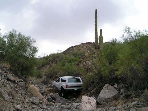 1993 Ford Bronco - A white 1993 Ford Bronco navigates a challenging rocky path in a desert landscape.