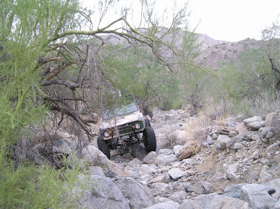 Off-road vehicle navigating a rocky trail with sparse desert vegetation