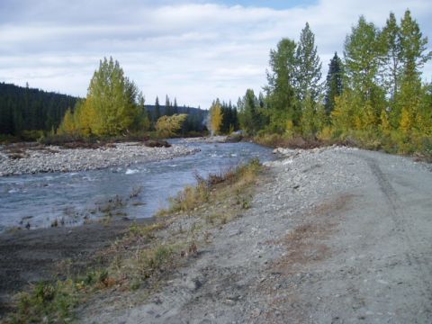 2000 Ford E350 - A dirt road runs alongside a river with trees in the background under a cloudy sky.