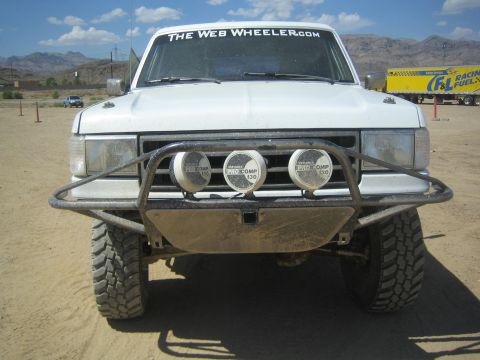 1990 Ford Bronco - front of a white off-road truck shows a tube brush guard, three Pro Comp driving lights and a Web Wheeler banner.