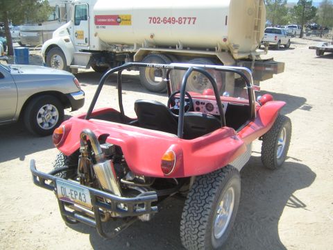 1990 Ford Bronco - rear of a red open dune buggy with chrome exhaust sits beside a fuel tanker truck in a dusty desert lot.