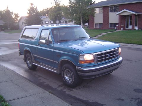 1995 Ford Bronco - A blue 1995 Ford Bronco, equipped with roof-mounted lights, is seen parked on the side of a street in a suburban neighborhood.