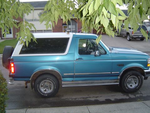 1995 Ford Bronco - Side view of a teal 1995 Ford Bronco XLT parked on a street with trees overhead.