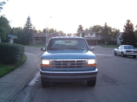 1995 Ford Bronco - Front view of a blue Ford Bronco parked on a suburban street with a white sedan in the background.