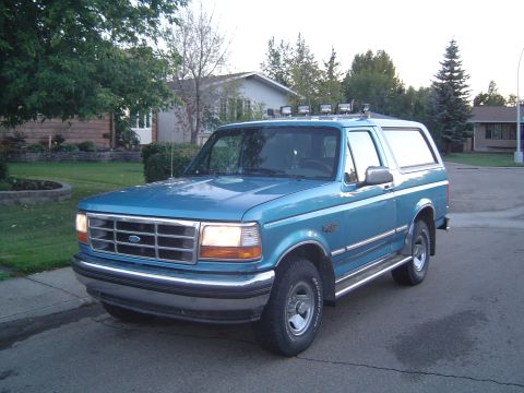 1995 Ford Bronco - A blue Ford Bronco is parked on a residential street, showing its front and side profile.