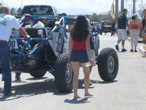1990 Ford Bronco - woman stands behind a blue number-200 tube-frame off-road buggy with large knobby tires as people mill about the pit.
