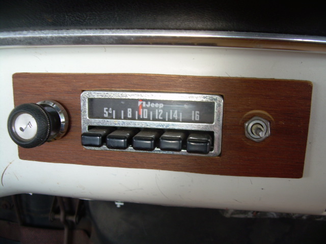 Vintage Jeep-branded AM push-button radio in wood panel on white dashboard with knob and toggle switch