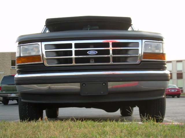 1992 Ford Bronco front grille and bumper, black soft top, chrome accents, parked on grass