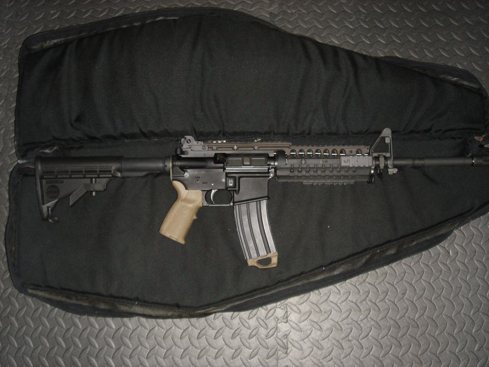 Assault rifle with tan grip and extended magazine lying in an open black gun case