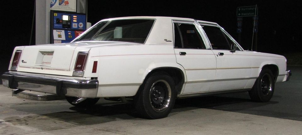 White sedan with a chrome bumper and rectangular taillights parked at a gas pump
