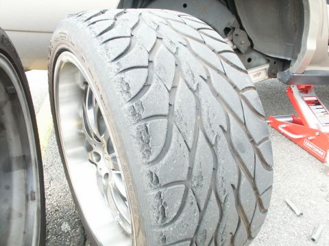 2001 Mercury Grand Marquis - Close-up of a worn tire on a custom rim, with a red hydraulic jack visible in the background.