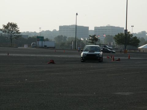 2001 Mercury Grand Marquis - A black Subaru WRX STI navigates a course marked by orange cones, with other vehicles and buildings in the background.