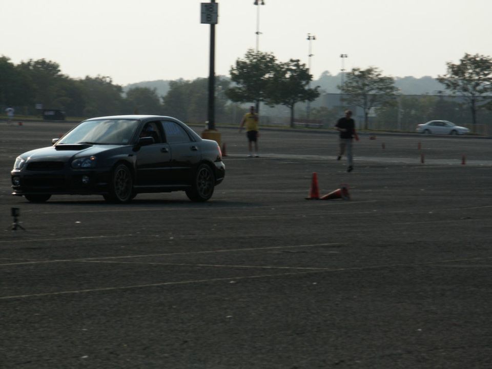 Black Subaru Impreza WRX sedan, 3/4 front view, on a track with cones