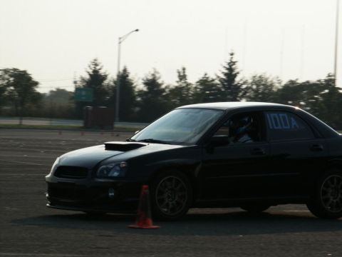 2001 Mercury Grand Marquis - Black Subaru Impreza WRX with hood scoop and racing numbers on window during an event.
