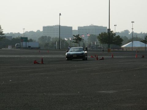 2001 Mercury Grand Marquis - A black Mazda Miata navigates a course marked by traffic cones in an open lot with buildings in the background.